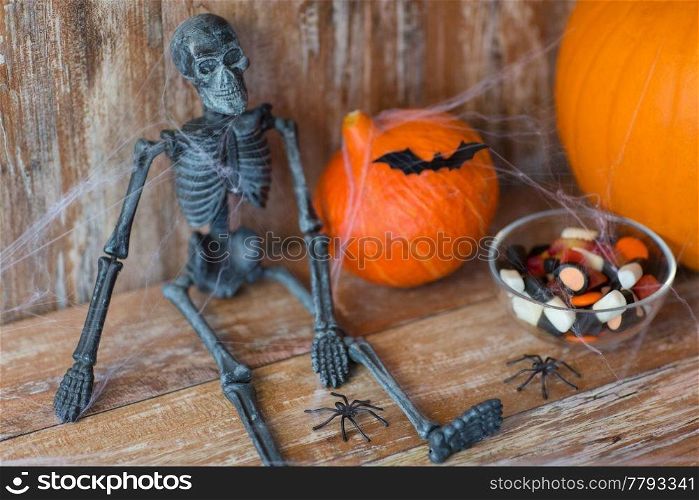 halloween, decorations and holidays concept - pumpkins with bats, skeleton and candies on wooden background. halloween pumpkins, skeleton and candies