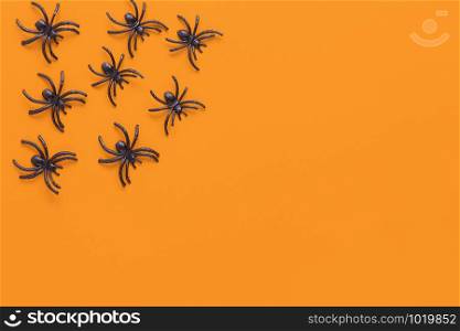 Halloween flat lay. Black spiders on orange background with copy space. Minimal style. Horizontal. Trick-or-treat concept.