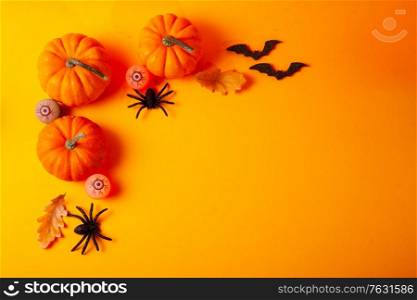 Halloween flat lay top view scene with pumpkins and spiders on orange background with copy space. Halloween scene on orange background