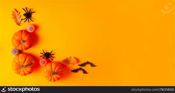 Halloween flat lay top view scene with pumpkins and spiders on orange background with copy space. Halloween scene on orange background