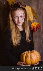 Halloween - girl in a suit with a pattern on her face and with a pumpkin