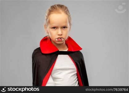 halloween, holiday and childhood concept - girl in black dracula costume with cape and fangs over grey background. girl in dracula costume with cape on halloween