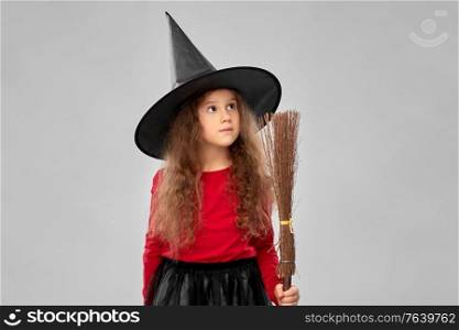 halloween, holiday and childhood concept - girl in costume and witch hat with broom over grey background. girl in black witch hat with broom on halloween
