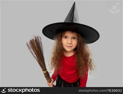 halloween, holiday and childhood concept - girl in costume and witch hat with broom over grey background. girl in black witch hat with broom on halloween