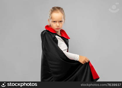 halloween, holiday and childhood concept - gloomy girl in black dracula costume with cape over grey background. girl in costume of dracula with cape on halloween