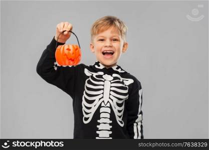 halloween, holiday and childhood concept - happy laughing boy in black costume with skeleton bones holding jack-o-lantern over grey background. happy boy in halloween costume with jack-o-lantern