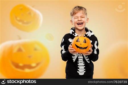 halloween, holiday and childhood concept - happy laughing boy in black costume with skeleton bones holding jack-o-lantern over pumpkins on background. happy boy in halloween costume with jack-o-lantern