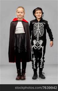 halloween, holiday and childhood concept - happy smiling boy and girl in costumes of dracula and skeleton over grey background. happy children in halloween costumes