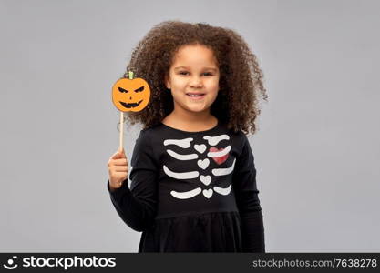halloween, holiday and childhood concept - smiling african american girl in black costume dress with skeleton bones and jack-o-lantern party accessory over grey background. girl in halloween costume with jack-o-lantern