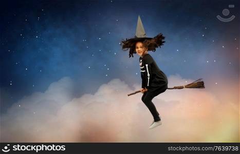 halloween, holiday and childhood concept - smiling african american girl in black costume dress and witch hat with broom over starry night sky and clouds on background. girl in black witch hat with broom on halloween
