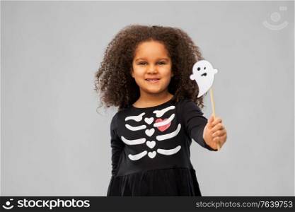halloween, holiday and childhood concept - smiling african american girl in black costume dress with skeleton bones and ghost over grey background. girl in black halloween dress with skeleton bones