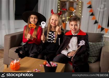 halloween, holiday and childhood concept - smiling boy and girls in costumes with party props and having fun at home. kids in halloween costumes having fun at home