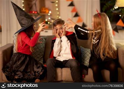 halloween, holiday and childhood concept - smiling boy and girls in costumes playing and scaring each other at home at night. kids in halloween costumes playing at home