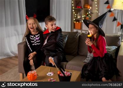halloween, holiday and childhood concept - smiling boy and girls in party costumes playing with flashlight and scaring each other at home. kids in halloween costumes playing at home