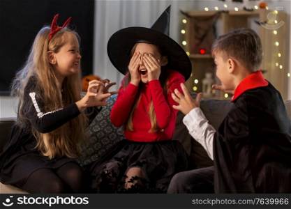 halloween, holiday and childhood concept - smiling boy and girls in party costumes playing and scaring each other at home at night. kids in halloween costumes playing at home