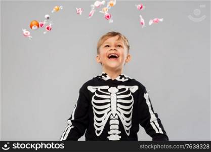 halloween, holiday and childhood concept - smiling boy in black costume of skeleton with candies trick-or-treating over grey background. boy with candies trick-or-treating on halloween