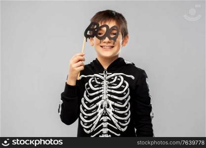 halloween, holiday and childhood concept - smiling boy in black costume of skeleton with boo party prop over grey background. boy in halloween costume of skeleton with props