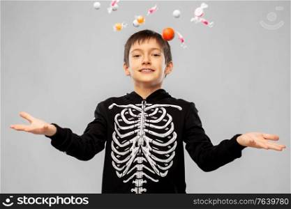 halloween, holiday and childhood concept - smiling boy in black costume of skeleton with candies over grey background. boy in halloween costume of skeleton with candies
