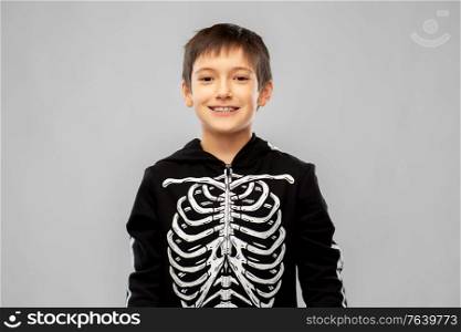 halloween, holiday and childhood concept - smiling boy in black costume of skeleton over grey background. boy in black halloween costume with skeleton bones
