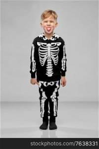 halloween, holiday and childhood concept - smiling boy in black costume with skeleton bones showing tongue over grey background. boy in black halloween costume with skeleton bones