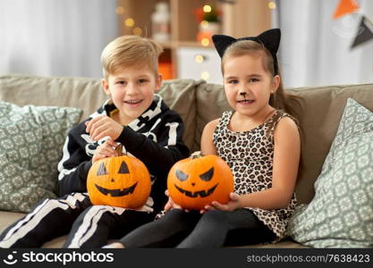 halloween, holiday and childhood concept - smiling little boy and girl in costumes with jack-o-lantern pumpkins having fun at home. kids in halloween costumes with pumpkins at home
