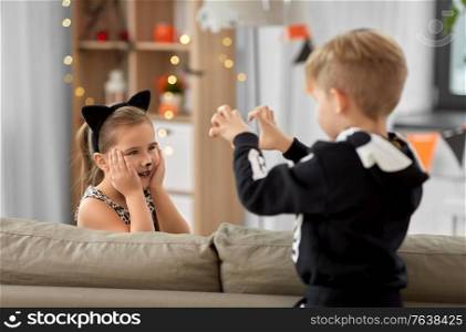 halloween, holiday and childhood concept - smiling little boy and girl in costumes playing and having fun at home. kids in halloween costumes playing at home