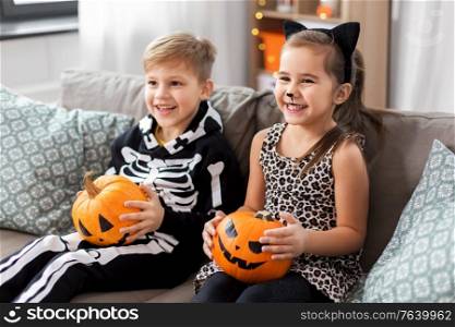 halloween, holiday and childhood concept - smiling little boy and girl in party costumes with jack-o-lantern pumpkins having fun at home. kids in halloween costumes with pumpkins at home