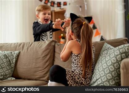 halloween, holiday and childhood concept - smiling little boy and girl in costumes having fun at home. kids in halloween costumes having fun at home