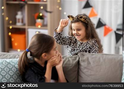 halloween, holiday and childhood concept - smiling little girls in costumes playing with toy spider at home. girls in halloween costumes playing with spider