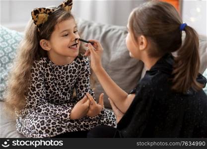 halloween, holiday and childhood concept - smiling little girls in party costumes doing face painting at home. girls doing face painting on halloween at home