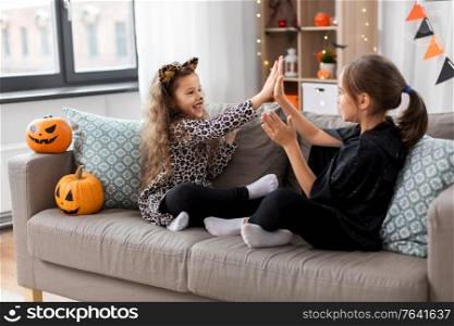 halloween, holiday and childhood concept - smiling little girls in party costumes playing clapping game at home. girls in halloween costumes playing game at home