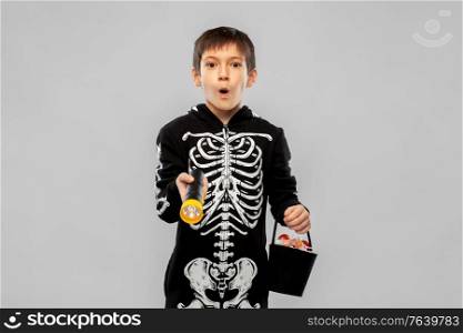 halloween, holiday and trick-or-treating concept - excited boy in black costume of skeleton with candies and flashlight over grey background. boy in halloween costume with candies and torch