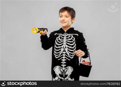 halloween, holiday and trick-or-treating concept - smiling boy in black costume of skeleton with candies and flashlight over grey background. boy in halloween costume with candies and torch