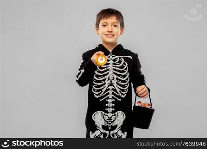 halloween, holiday and trick-or-treating concept - smiling boy in black costume of skeleton with candies and flashlight over grey background. boy in halloween costume with candies and torch