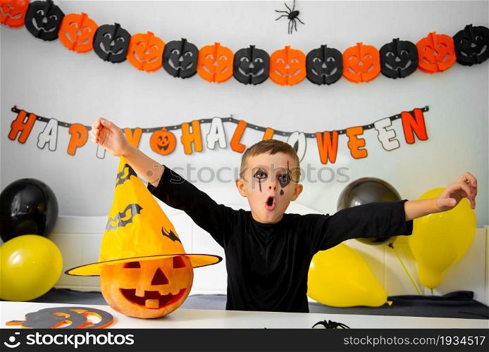 Halloween holiday concept. Cute boy in costume sitting behind a table in Halloween theme decorated room. Halloween with safety measures from Covid-19. Halloween holiday concept. Cute boy in costume sitting behind a table in Halloween theme decorated room.