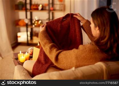 halloween, holidays and leisure concept - young woman taking woolen cardigan from shopping bag at cozy home. woman taking cardigan from shopping bag at home