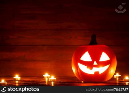 Halloween Jack o Lantern pumpkin head and burning candles on wooden background. Halloween lantern pumpkin and candles