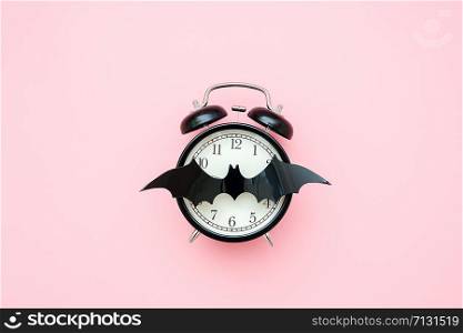 Halloween night concept. Black alarm clock and bat on face clock on pink background. Creative flat lay, top view, copy space, template for yuor design, greeting card, invitation.. Halloween night concept. Black alarm clock and bat on face clock on pink background. Creative flat lay, top view, copy space, template for yuor design, greeting card, invitation