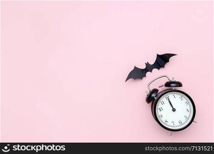 Halloween night concept. Black alarm clock and flying bat on pink background. Creative flat lay, top view, copy space, template for yuor design, greeting card, invitation.. Halloween night concept. Black alarm clock and flying bat on pink background. Creative flat lay, top view, copy space, template for yuor design, greeting card, invitation