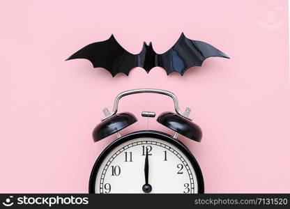 Halloween night concept. Black alarm clock and flying bat on pink background, closeup. Creative flat lay, top view, template for yuor design, greeting card, invitation.. Halloween night concept. Black alarm clock and flying bat on pink background, closeup. Creative flat lay, top view, template for yuor design, greeting card, invitation