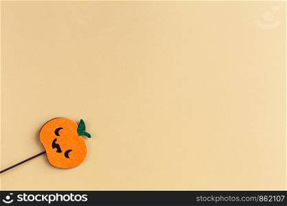 Halloween party accessory, shiny pumpkin with cute creepy faces. Pastel yellow background, place for text. Holiday flat lay. Minimal style. Horizontal.