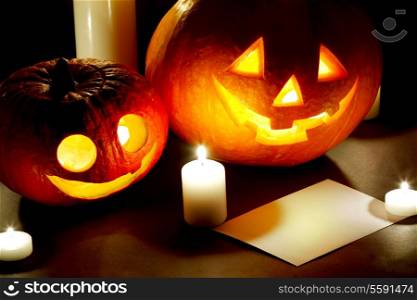 Halloween pumkins, candles and postcard on dark background