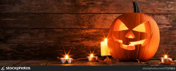 Halloween pumpkin glowing jack o lantern with carved face and candles on wooden background, banner with copy space for text. Halloween pumpkin and candles