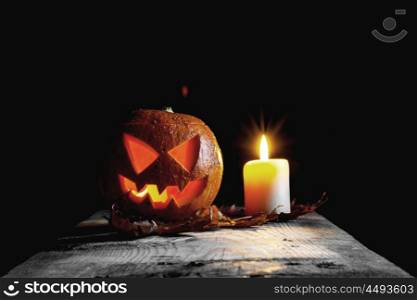 Halloween pumpkin head. Halloween pumpkin head and candle on wooden table over black background