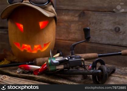 halloween pumpkin head in heat and eyeglass with fishing tackles on wooden boards background