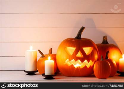 Halloween pumpkin head jack lantern and candles on light wooden background. Halloween pumpkin and candles