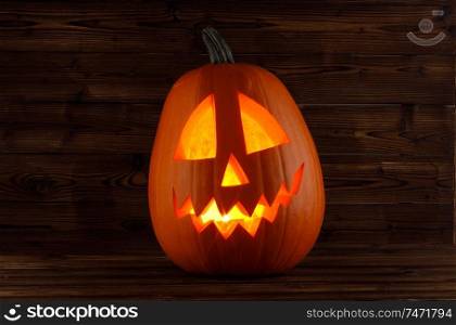 Halloween pumpkin head jack o lantern with candle inside on wooden background. Halloween pumpkin glowing