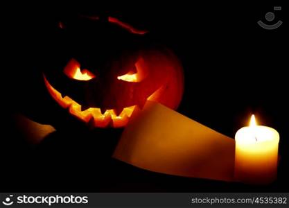 Halloween pumpkin with blank post card and candle on black background