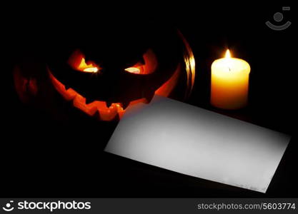 Halloween pumpkin with blank post card and candle on black background