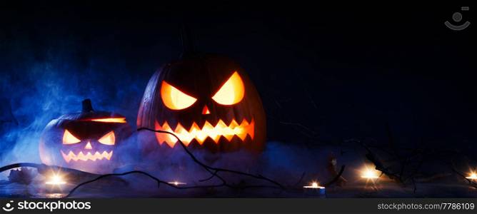 Halloween pumpkins head jack o lantern and candles in blue light and mist. Halloween pumpkins and candles